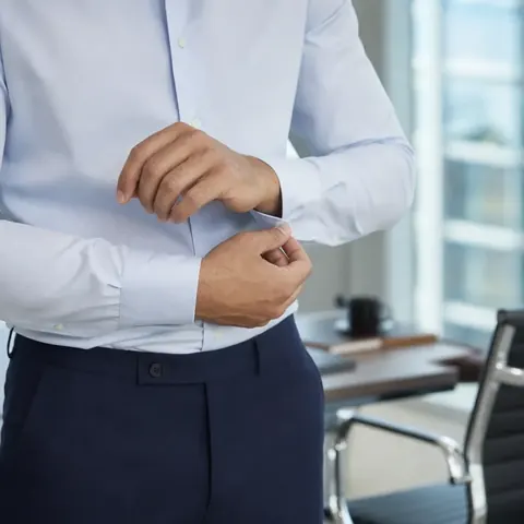 Homem de camisa azul-clara e calça social ajustando o punho no escritório